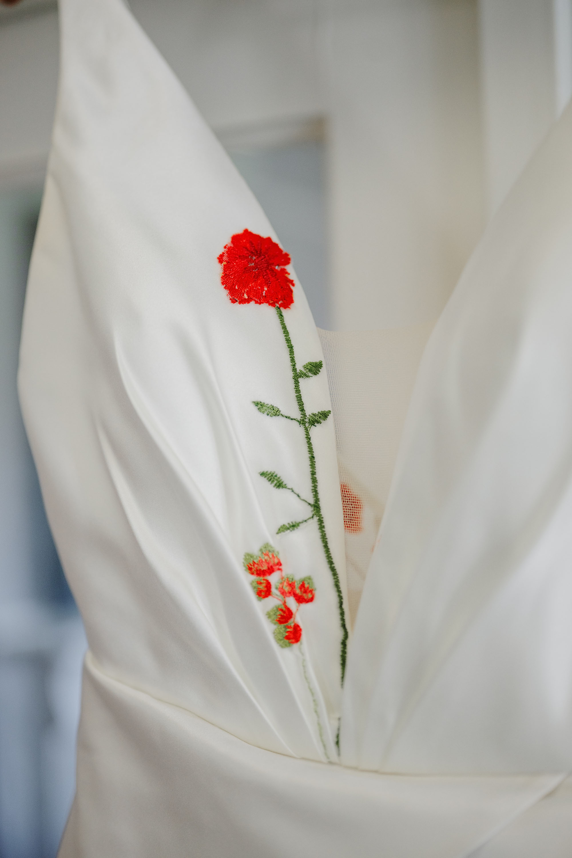 wedding photograph closeup of wedding dress with embroidered red flower on front of white gown