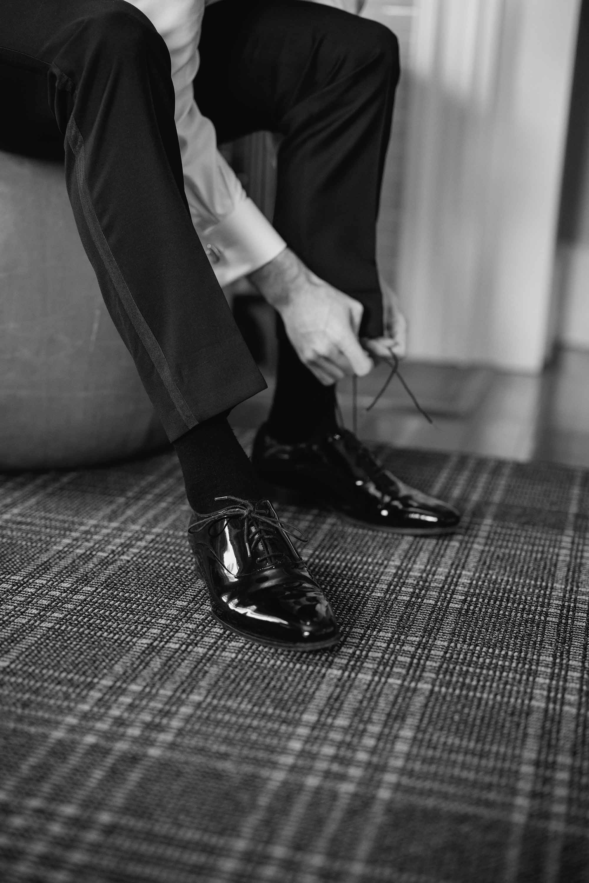 wedding photographs of groom putting on wedding ceremony shoes, black and white photo